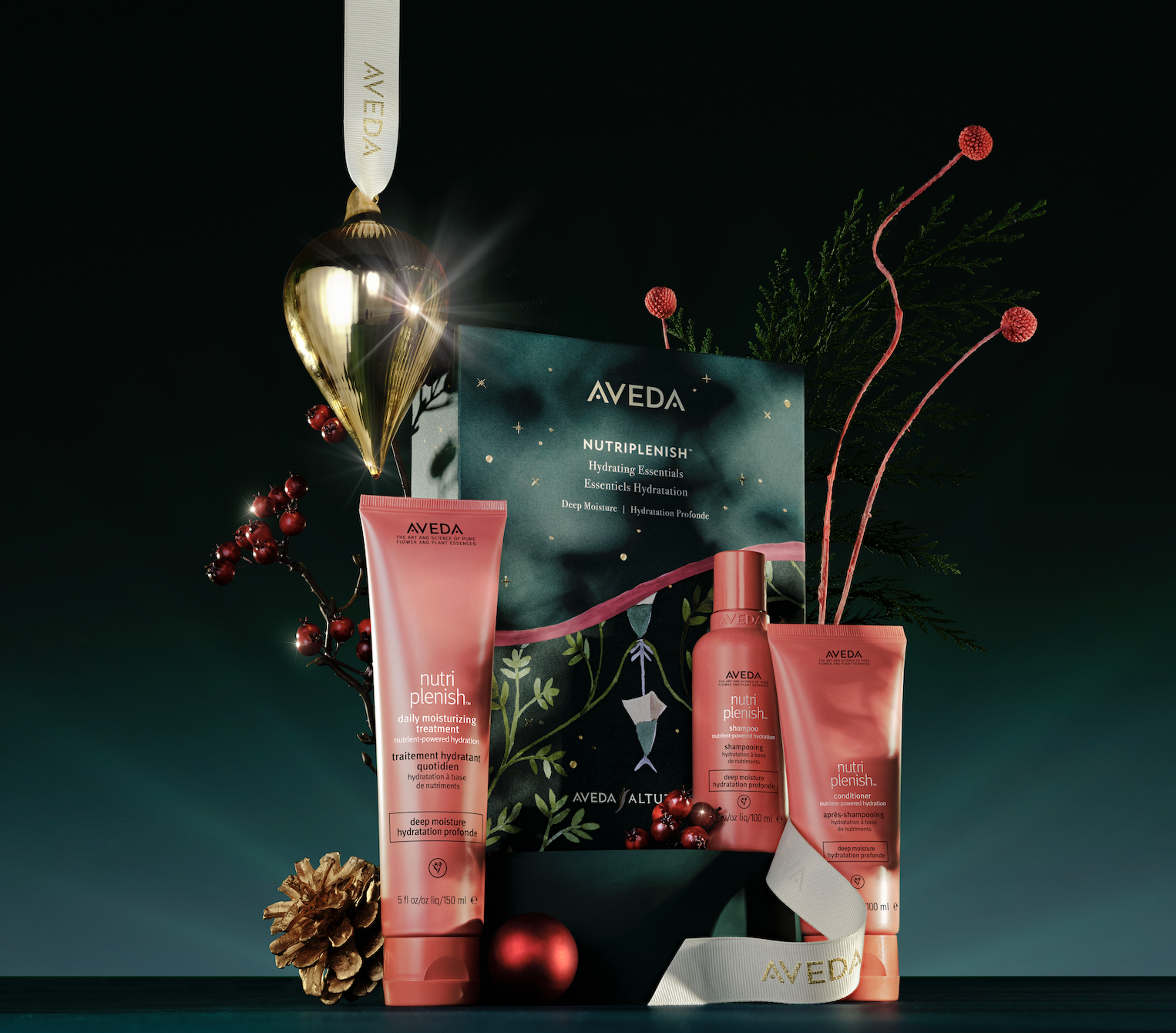 Aveda NutriPlenish holiday gift set with three hair care products displayed with festive ornaments and greenery on a dark background.