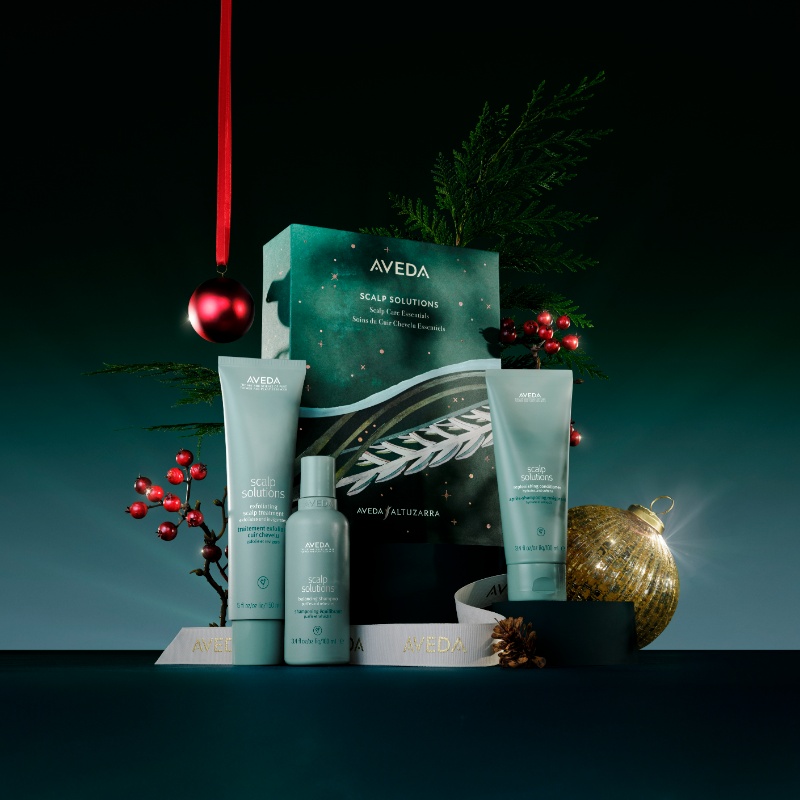 Aveda Scalp Solutions gift set displayed with festive decorations, including a red bauble, gold ornament, and greenery, against a dark background.